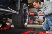 A person using a red CRAFTSMAN cordless impact wrench to loosen or tighten lug nuts on a car wheel. The person is wearing